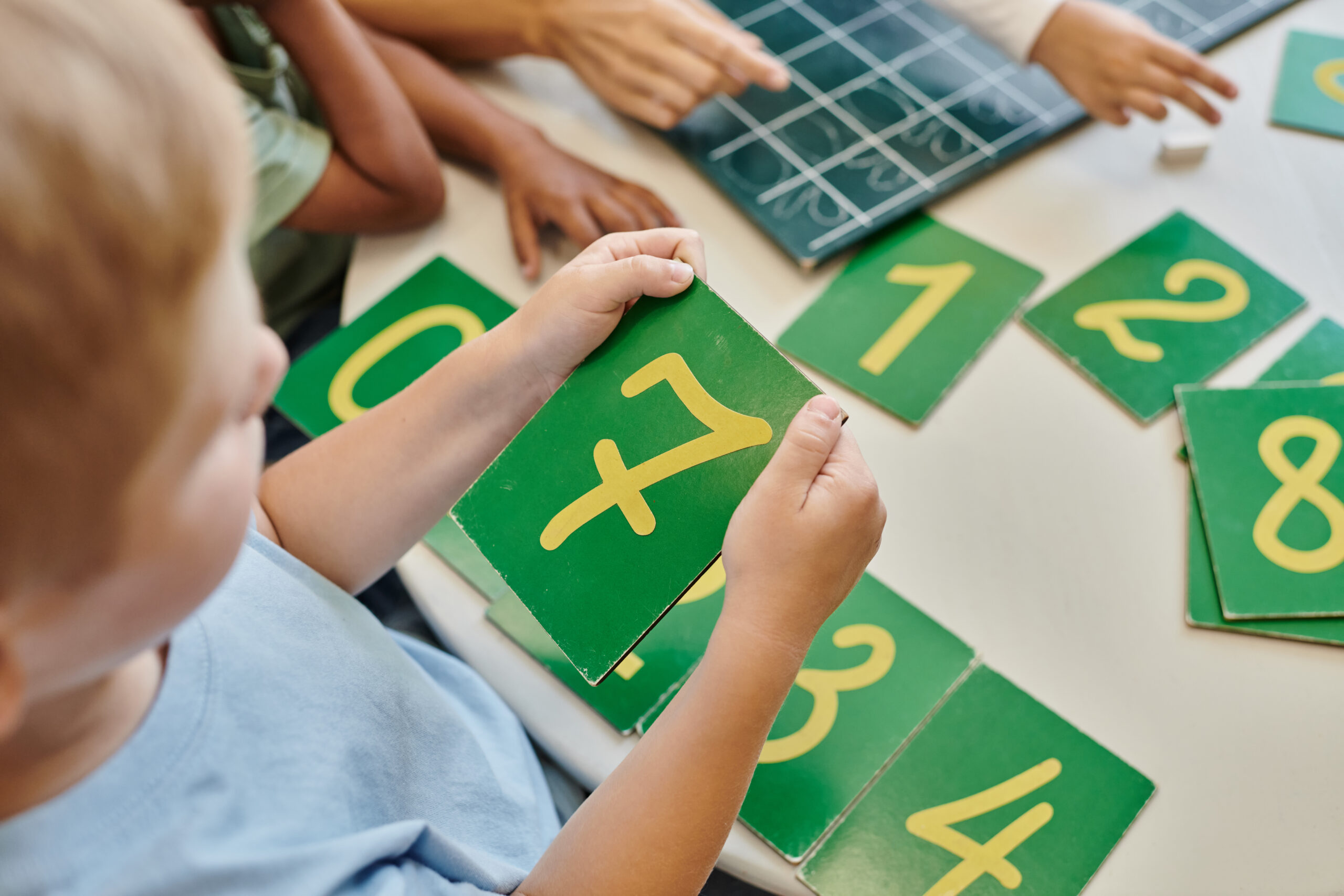 top view of boy holding number seven card, learning how to count in Montessori school, study